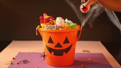 Halloween Jack o Lantern orange bucket with candy. Child kid hand take a one candy.