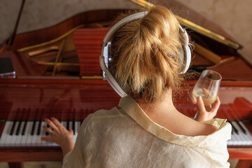 A girl with a glass of wine is sitting near the piano. The concept of loneliness