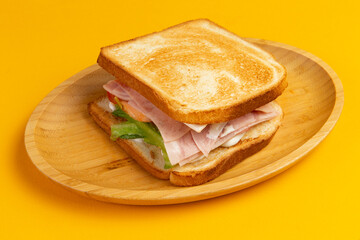 Sandwich with ham and salad in a wooden plate.