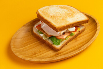 Sandwich with ham and salad in a wooden plate.