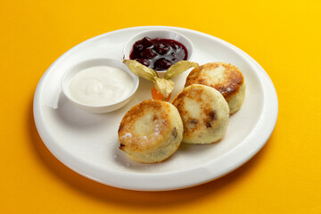 Traditional breakfast syrniki in a plate on a yellow background.