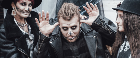 Scary family, mother, father, daughters celebrating halloween. Terrifying black skull half-face makeup and witch costumes, stylish images.Horror,fun at children's party in barn on street.Hats,jackets