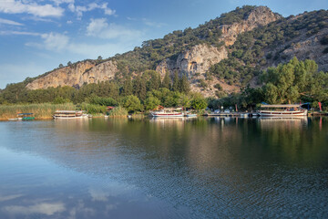Fototapeta premium The rock-cut temple tombs of the ancient city of Kaunos in Dalyan, Muğla, Turkey. Beautiful view of Dalyan river with reed beds, excursion boats and carved tombs in the background.