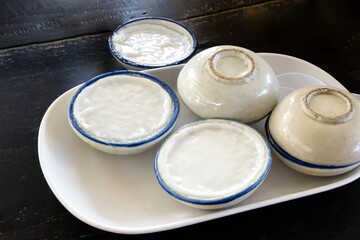 Thai dessert Khanom thuai, sweet, fragrant, coconut milk flavor Made from rice flour, coconut milk and sugar, steamed in ceramic cup and topped with coconut milk. Thai dessert in a white plate.