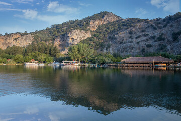 Obraz premium The rock-cut temple tombs of the ancient city of Kaunos in Dalyan, Muğla, Turkey. Beautiful view of Dalyan river with reed beds, excursion boats and carved tombs in the background.