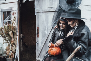 Fototapeta na wymiar Scary family,mother,daughter celebrating halloween. Street barn. Pumpkin jack-o-lantern.Terrifying black skull half-face makeup and witch costumes, broom,stylish images hat, jackets. Children's party