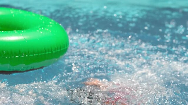 funny boy trying to get into the center of colorful swim ring in swimming pool on summer day. boy missed and flew past the swim ring