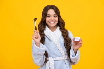 Beauty, make up and kids cosmetics. Teenage girl with brush applying blush to face isolated on yellow studio background.