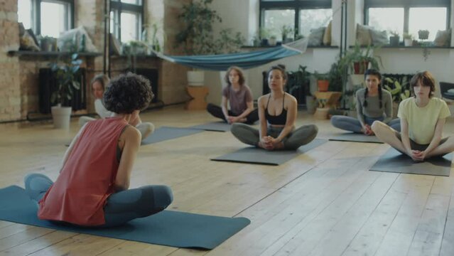 Group of sporty girls practicing butterfly stretch on mats in studio during yoga class with female teacher