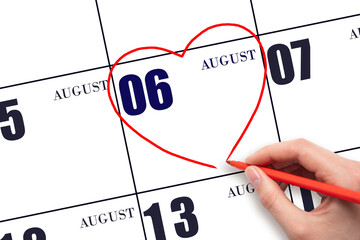 A woman's hand drawing a red heart shape on the calendar date of 6 August. Heart as a symbol of...