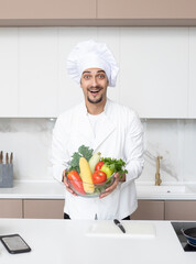 Close up of smiling and happy male chef holding a bowl full of fruits and vegetables in the kitchen. Healthy food concept	