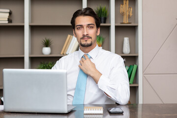 Portrait of young positive and confident handsome business man working on laptop in the modern office