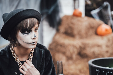 Beautiful scary little girl celebrating halloween. Terrifying black, white half-face makeup and...