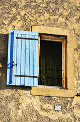 front view, medium distance of a barred window with blue, wood, shutter, on a 1300's century building, in France
