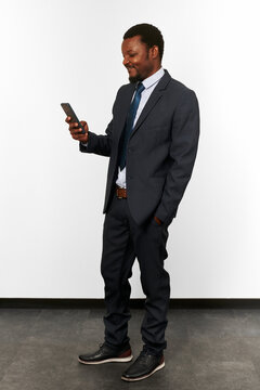 Smiling african american black man in business suit looking in smartphone white wall background. Full size portrait of happy black businessman with phone in hand satisfied with good deal
