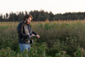 Young worried farmer writes notes while standing against the background of a blurred corn field