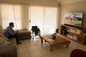 Caucasian man watching tv with football match on screen