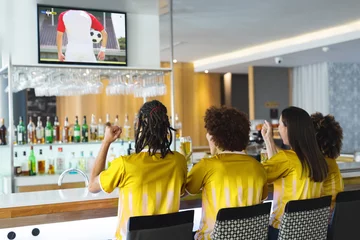 Tuinposter Diverse friends supporting and watching tv in bar with football match on screen © vectorfusionart