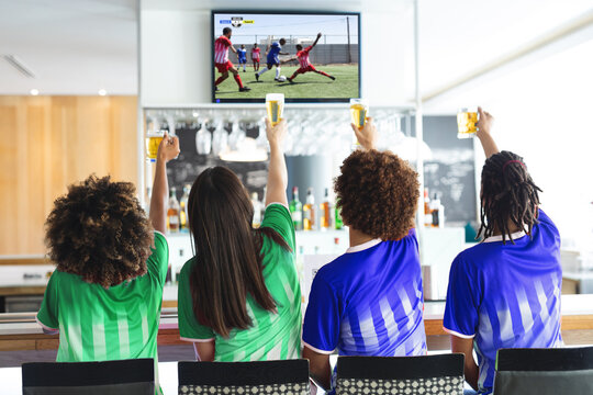 Diverse friends supporting and watching tv in bar with football match on screen