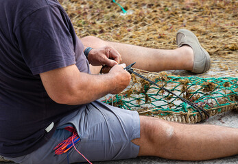 Pescador arreglando su red de pesca en el puerto de Cala Figuera, junto al pueblo de Santanyí, en la isla de Mallorca (Islas Baleares, España). - obrazy, fototapety, plakaty