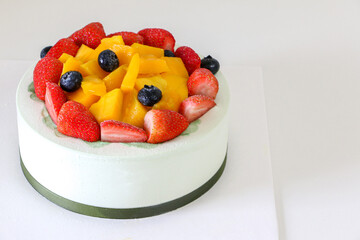 Delicious fruity birthday cake filled with fresh strawberries, blueberries and mango on top, on left of frame and white table