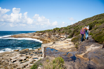 People walking on hiking track with beautiful ocean and rocky sandstone coastline view. Travel destination. Royal National Park, NSW, Australia. Jibbon Loop Track © Daria Nipot