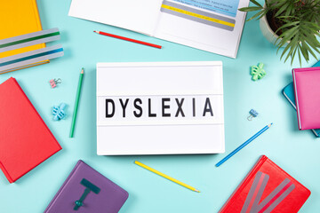 Dyslexia awareness, help children with reading, learning difficulties concept. Lightbox with DYSLEXIA word, colorful books and open book with reading highlight bookmark overlays strips. Top view
