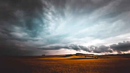 Time lapse of a sunset, dark clouds move away over the golden farmer's field in countryside