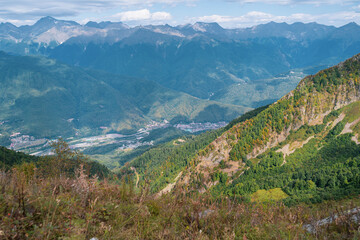 Fototapeta na wymiar Alpine Meadows Trail, Krasnaya Polyana Resort. Alpine Meadows Walking Route. Aerial view of the green mountain valley, surrounded by high mountains.