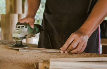 Asian carpenter is sanding wood using an electric wood sander to smooth the wood surface on a workbench at his factory. Small Business , working as your own boss at home Concept