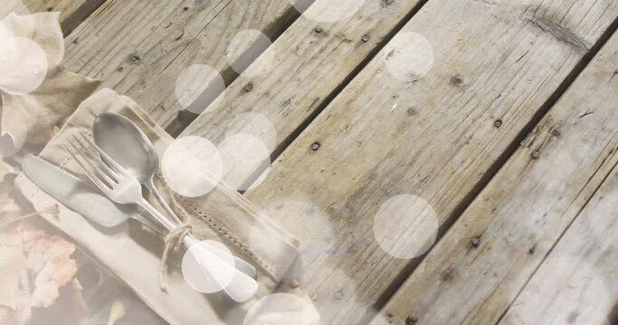 Animation of light spots over cutlery and leaves on wooden background