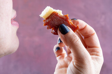 Closeup of woman's hand taking slices of guava sweet and cheese to her mouth.