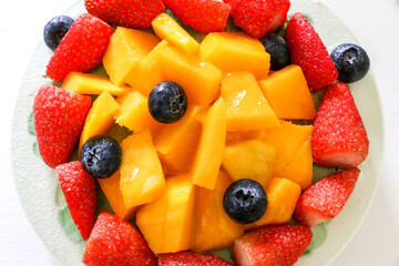 Top view close up of fresh fruits, strawberries, mango and blueberries topping a birthday cake