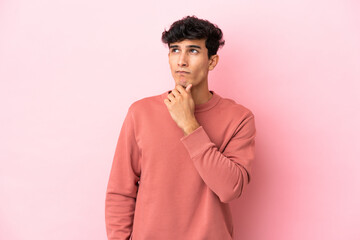 Young Argentinian man isolated on pink background having doubts