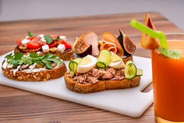 Four types of bruschetta with different fillings and a glass of juice with a peach.