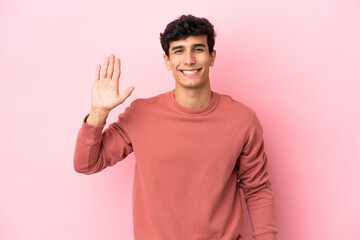Young Argentinian man isolated on pink background saluting with hand with happy expression