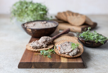 Homemade meat or chicken liver pate with multigrain crackers and microgreen, light concrete background.