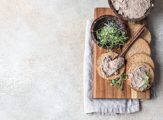 Fototapeta na wymiar Homemade meat or chicken liver pate with multigrain crackers and microgreen, light concrete background. Top view.