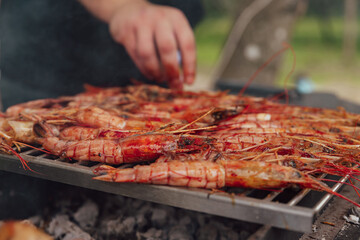 Man cooks large shrimp langoustines on an open fire on the grill with smoke. BBQ outdoor. Grilled...