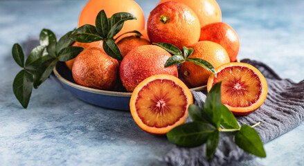Ripe juicy Sicilian blood oranges with leaves on a ceramic plate, blue concrete background.