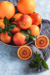 Ripe juicy Sicilian blood oranges with leaves on a ceramic plate, blue concrete background.