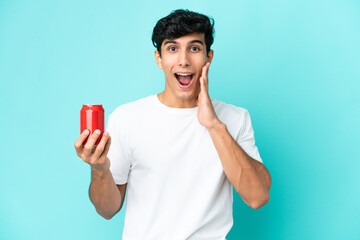 Young Argentinian man holding a refreshment isolated on blue background with surprise and shocked facial expression