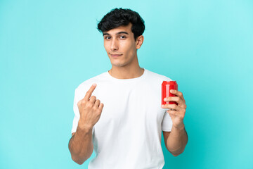 Young Argentinian man holding a refreshment isolated on blue background doing coming gesture