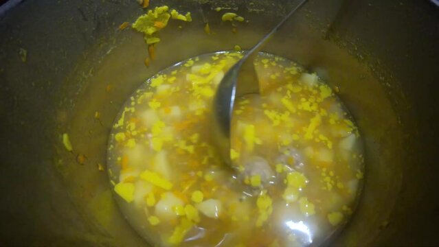 yellow soup with meatballs potatoes and vegetables in a gray pot and plate stirs with a spoon and ladle delicious food