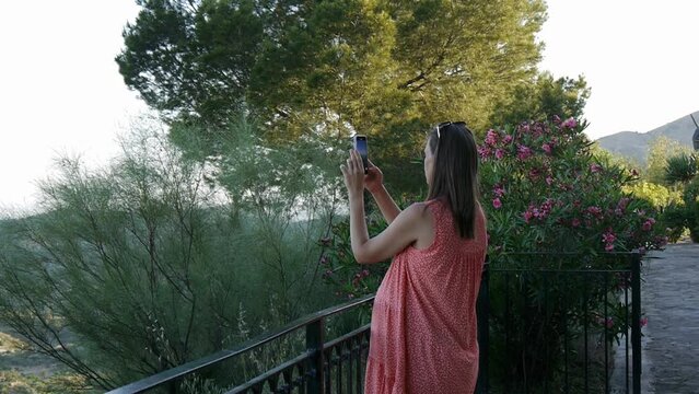Young pregnant woman wearing summer dress taking pictures on the phone. Medium shot.