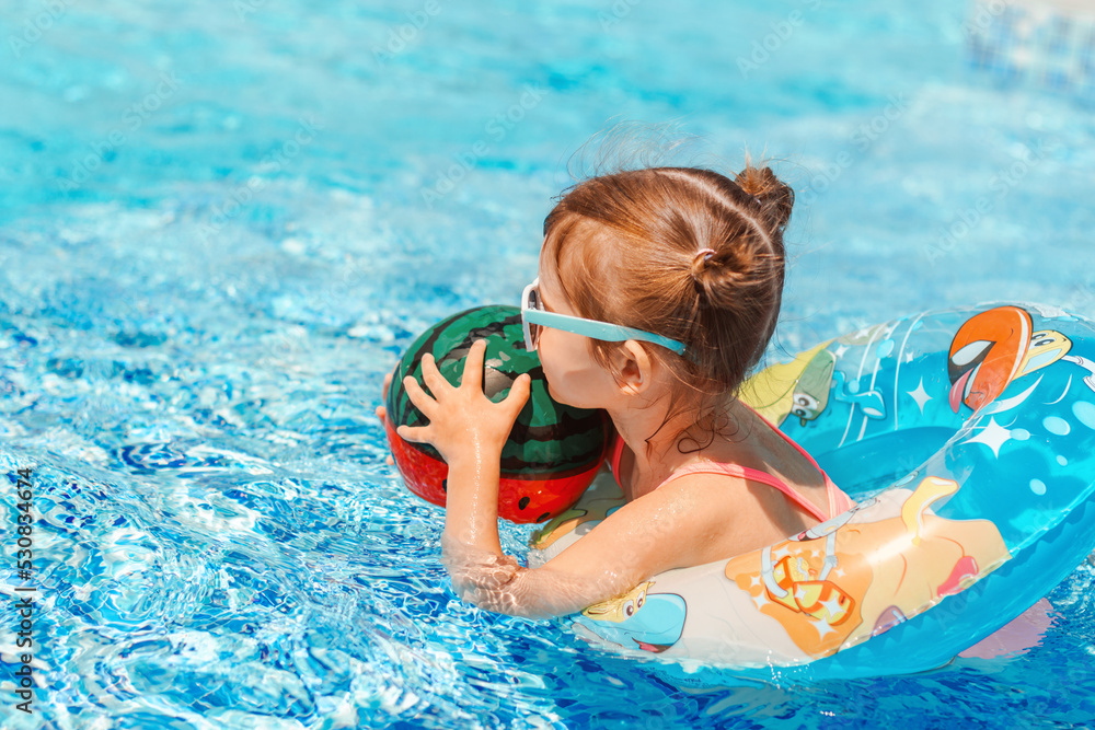 Wall mural cute toddler girl wear sunglasses having fun in swimming pool with blue clean water. family vacation