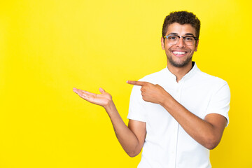 Young handsome Brazilian man isolated on yellow background holding copyspace imaginary on the palm...