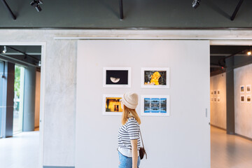 Woman visiting art gallery her looking pictures on wall watching photo frame painting at artwork...