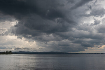 Dark heavy thunderstorm clouds over a lake surface. Thunder storm, active weather concept.