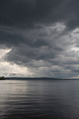 Fototapeta premium Dark heavy thunderstorm clouds over a lake surface. Thunder storm, active weather concept.